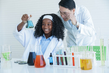 African American kid scientist and Asian teacher man looking chemical liquid for experiment at laboratory school. White background