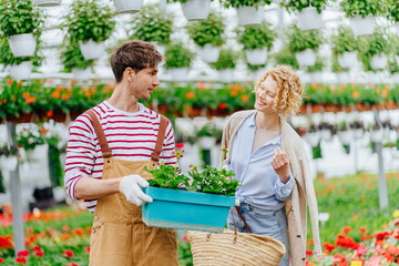 Fototapeta na wymiar Customer service in the plant store concept. Flower seller man helping female buyer to choosing plants in box for balcony female customer in garden centre or greenhouse.