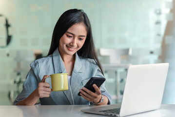 Asian businesswoman holding a coffee mug and smartphone at office.