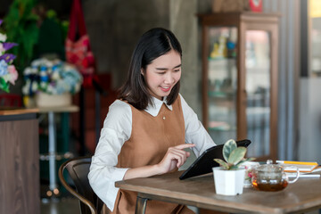 Asian woman sitting in a café spending free time relaxing by tablet at the café.