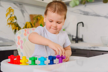 Child boy 2 y.o. plays with plastic colored shaped large screws and nuts, learning through the game.