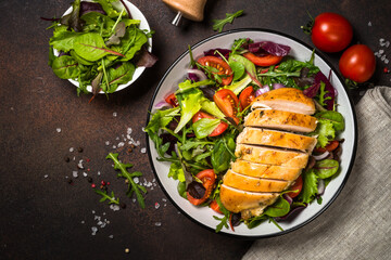 Fresh salad with baked chicken breast at dark kitchen table. Healthy food, clean eating concept. Top view image.