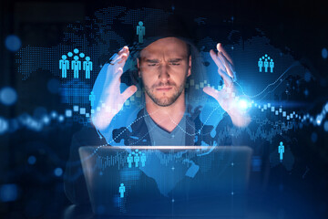 Handsome businessman in hoodie at workplace working with laptop to hire new employees for international business consulting. HR, social media hologram icons over office background