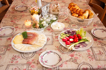 Lovely kitchen or dining room table with Easter breakfast meal. Cheese, eggs, ham, vegetables, baked food, with nice floral pattern plates and ornaments.