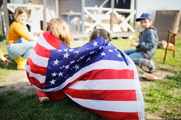American children wrapped themselves in the USA flag on Independence Day. Children sit by the fire...