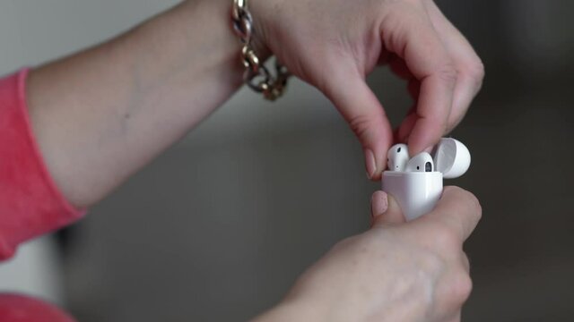close-up of a woman's hands taking out a wireless ear phones from charging box