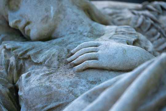 Fragment of an ancient statue of end of human life. Beautiful dead woman light on the bed. Selective focus on hand. Horizontal image.