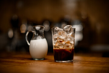 close-up of transparent glass with black coffee and ice cubes stands on table