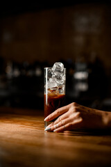 view of glass with cold black coffee and ice cubes and woman's hand holding it