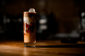 transparent glass with cold black coffee and milk on table