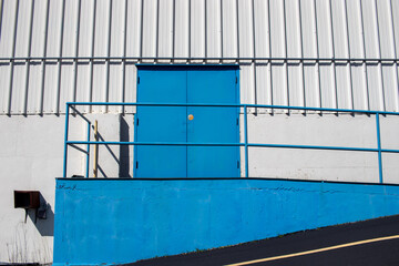 Blue double doors on ramp on white building exterior