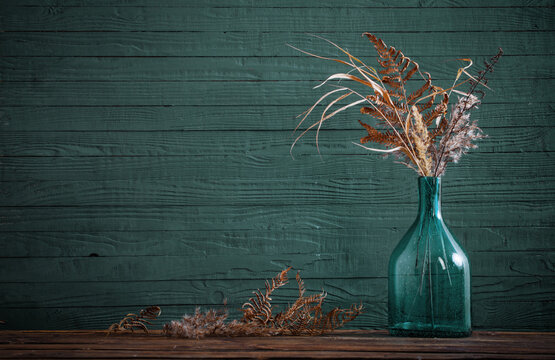 dried flowers in glass vase on wooden table on blue  background