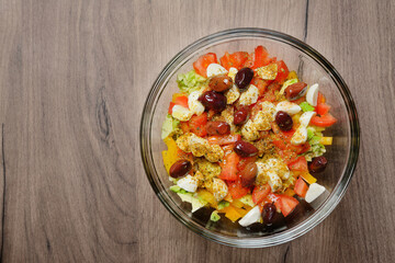 Greek salad with cheese, vegetables and olives in a glass bowl, on a wooden table. Top view