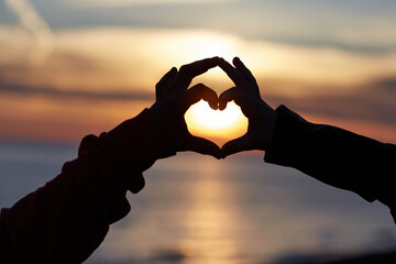 Heart shape with hands of loving couple on sunset sky background