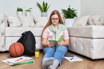 Teenage girl sitting at home on the living room floor reading book