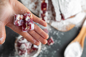 A woman is holding a dice shaped piece of fruit and nut flavored homemade Turkish delight covered...