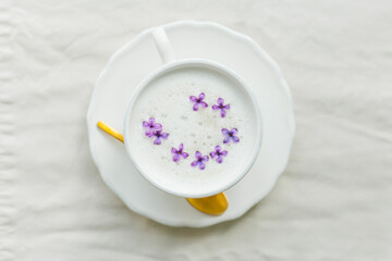 Fototapeta na wymiar Mug of cappuccino on a beige background. Lilac flowers. Rest at home. Quarantine.