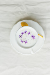 Mug of cappuccino on a beige background. Lilac flowers. Rest at home. Quarantine.