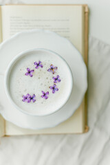 Mug of cappuccino on a beige background. Lilac flowers, book. Rest at home. Quarantine.