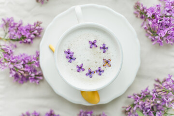 Mug of cappuccino on a beige background. Lilac flowers. Rest at home. Quarantine.