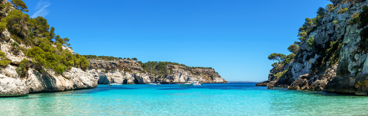 Panoramic view from an empty Cala Macarelleta, with turquoise waters and blue sky, in Menorca,...