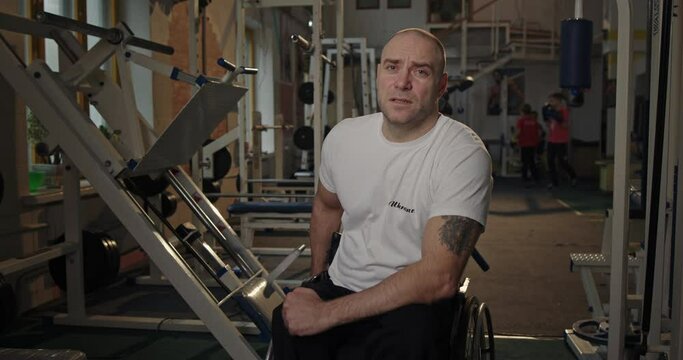 A man looks into the camera with a serious focused gaze Paralympian with defective legs not sitting legs in a wheelchair in the gym