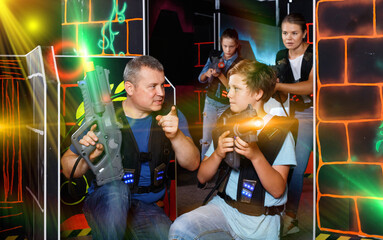 Fototapeta na wymiar Happy glad cheerful positive smiling teen boy with laser gun having fun on lasertag arena with his father