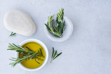 Bowl of essential oil with fresh rosemary twigs and a cleaning cushion on a light surface