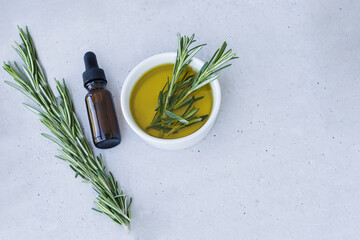 Bottle of essential oil with fresh rosemary twigs on a light surface