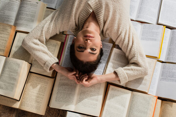 top view of pretty woman lying on pile of open books