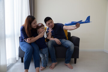 Asian family and 3 year old son having fun with toy plane and sitting on sofa in living room at home