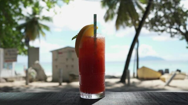 A misted glass with a fruity cocktail and the addition of rum stands on a bar counter against the backdrop of the ocean in the Seychelles.