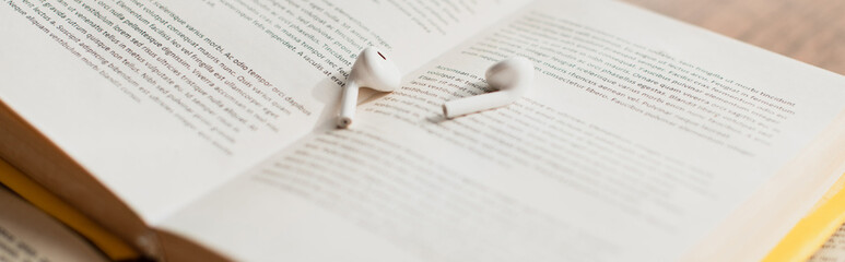 Fototapeta premium white wireless earphones on blurred book, banner