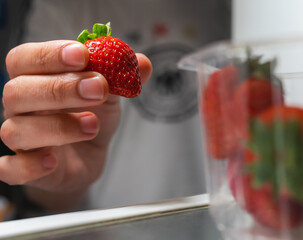 A person removes a strawberry from inside a package in a refrigerator.