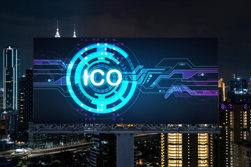 ICO hologram icon on billboard over panorama city view of Kuala Lumpur at night. KL is the hub of blockchain projects in Malaysia, Asia. The concept of initial coin offering, decentralized finance