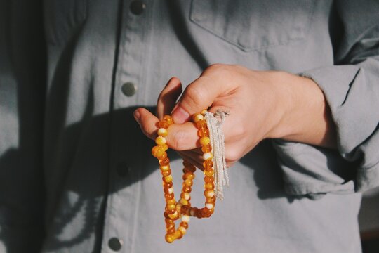 hand of muslim man performing islamic ritual chanting / invocation / dhikr (one hand) with orange rosary 