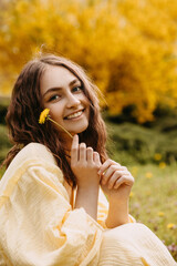 Happy young woman sitting in a garden, holding a dandelion.