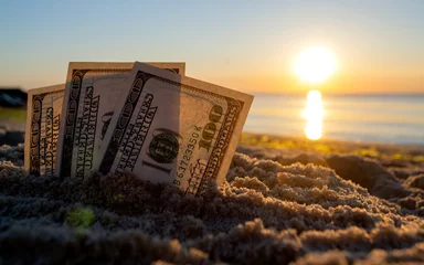 Foto op Plexiglas Three dollar bills are buried in sand on sandy beach near sea at sunset dawn © mari1408