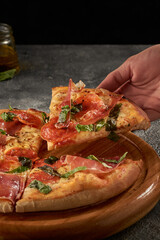 Vertical shot of a hand grabbing a piece of delicious prosciutto pizza