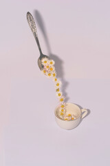 A spoon from which flowers are poured into a white cup. Chamomile flowers The concept of a healthy drink. Isolated on white matter.