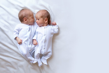Newborn twins on the bed, in the arms of their parents, on a white background. Life style, emotions...