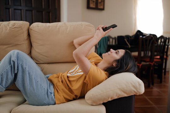 Side view of young female taking self portrait on cellphone while lying down on couch in living room