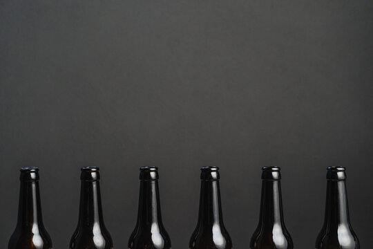 Row of identical dark bottles of alcoholic drinks with shiny surface on gray background