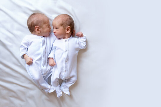 Newborn twins on the bed, in the arms of their parents, on a white background. Life style, emotions of kids.