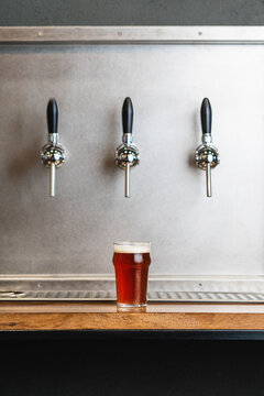 Beer with foam in glass jug against row of taps in bar on gray background
