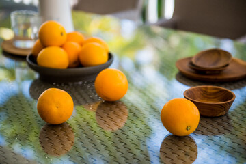 High angle of ripe fresh mandarins scattered on wicker table with glass top near wooden bowls on veranda on sunny day