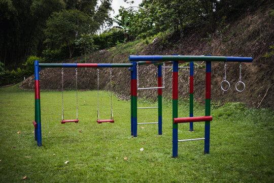 Multicolored playground playset with swings and climbing equipment located on grassy meadow in green park in Armenia Colombia - Powered by Adobe