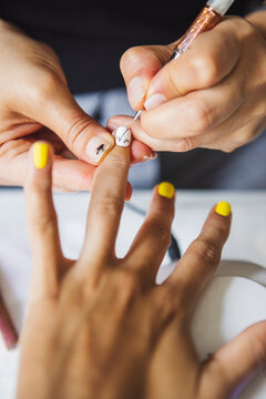 From above of crop unrecognizable manicurist doing nail art fpr female client in beauty salon in daylight