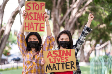 Ethnic females in masks holding posters protesting against racism in city street and looking at camera