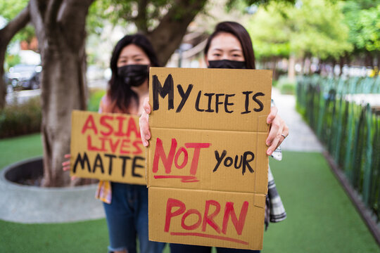 Ethnic females in masks holding posters protesting against racism in city street and looking at camera